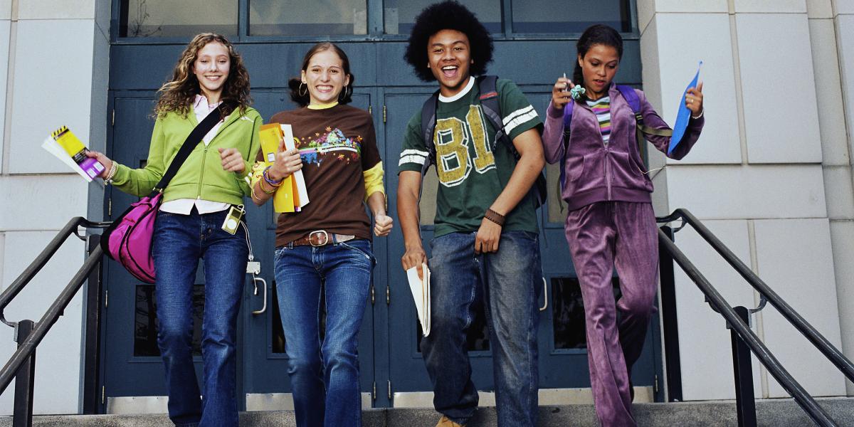 4 young teens leaving school with books and backpacks, all smiling