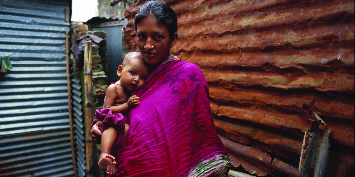  mother in Bangladesh wearing a magenta scarf holds her infant on her hip