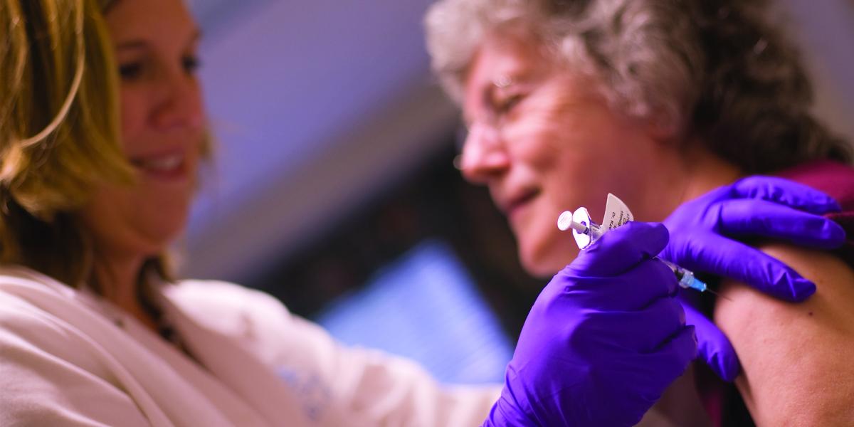 a nurse wearing purple gloves prepares to vaccinate an older adult woman
