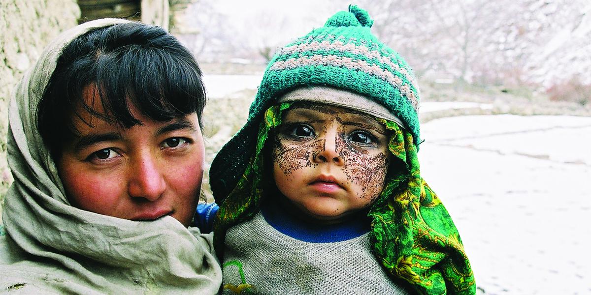 A mother holding her son, who wears a knit cap and a paste on his face as protection from the cold