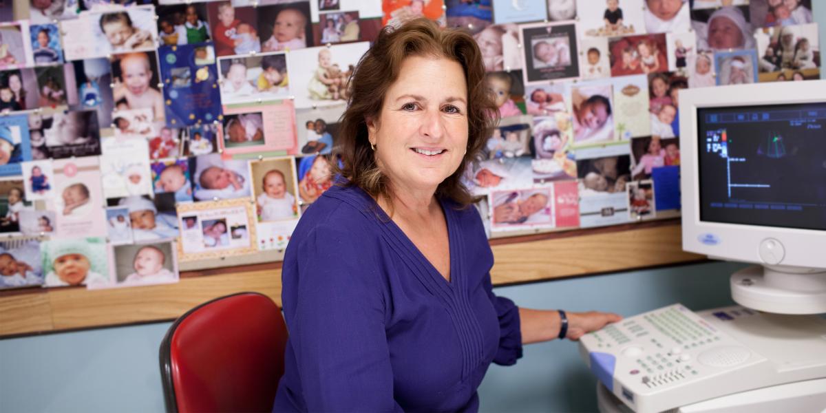 Janet DiPietro with a corkboard filled with baby pictures behind her