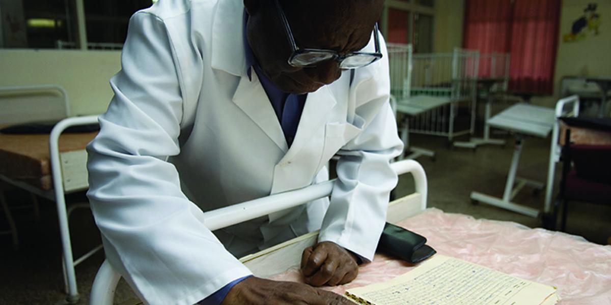 Clinician Redson Makasa, wearing a lab coat, reviews a paper ledger of measles cases