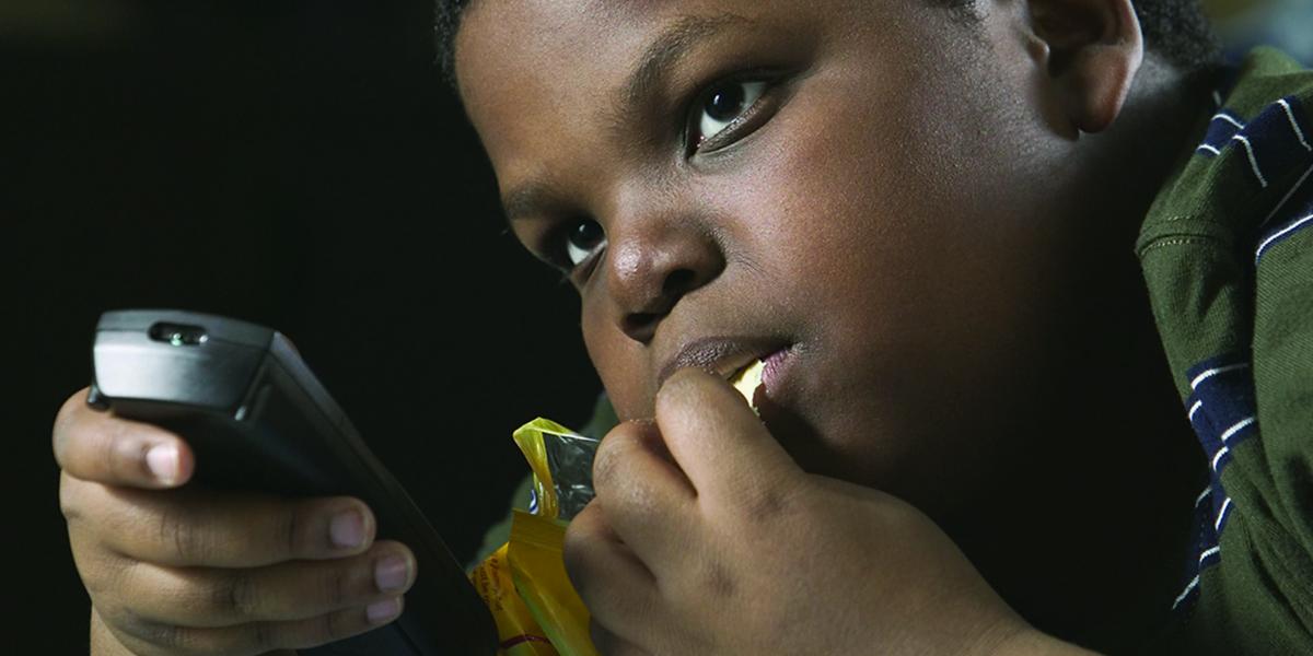 A young boy snacks on chips with a TV remote in his hand