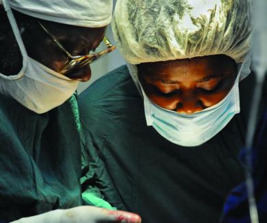 Dr. James Boima and a surgical nurse, both in surgical masks and caps, during a procedure