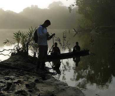 a researcher uses a G.I.S. device at the edge of the Amazon, where two children sit