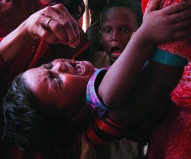 a crying Nepalese child is held with his head back to receive vitamin A drops in his mouth