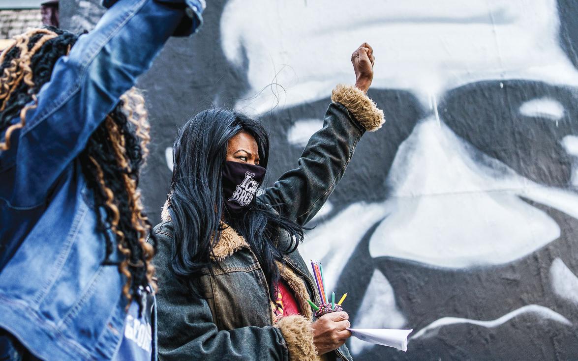 Black women in front of a George Floyd mural with raised fists.